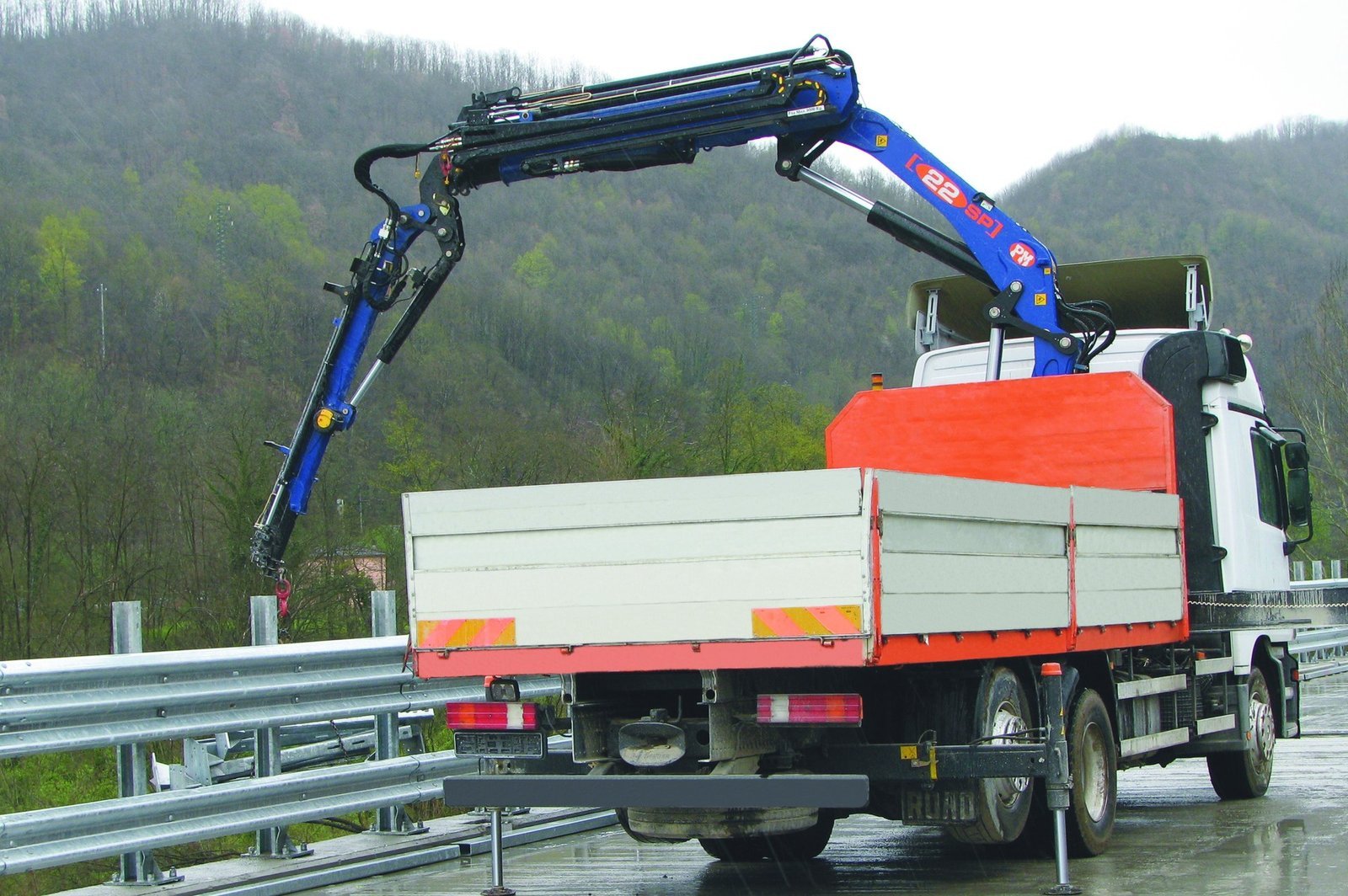 PM knuckle boom crane mounted behind the cab of a flat bed truck